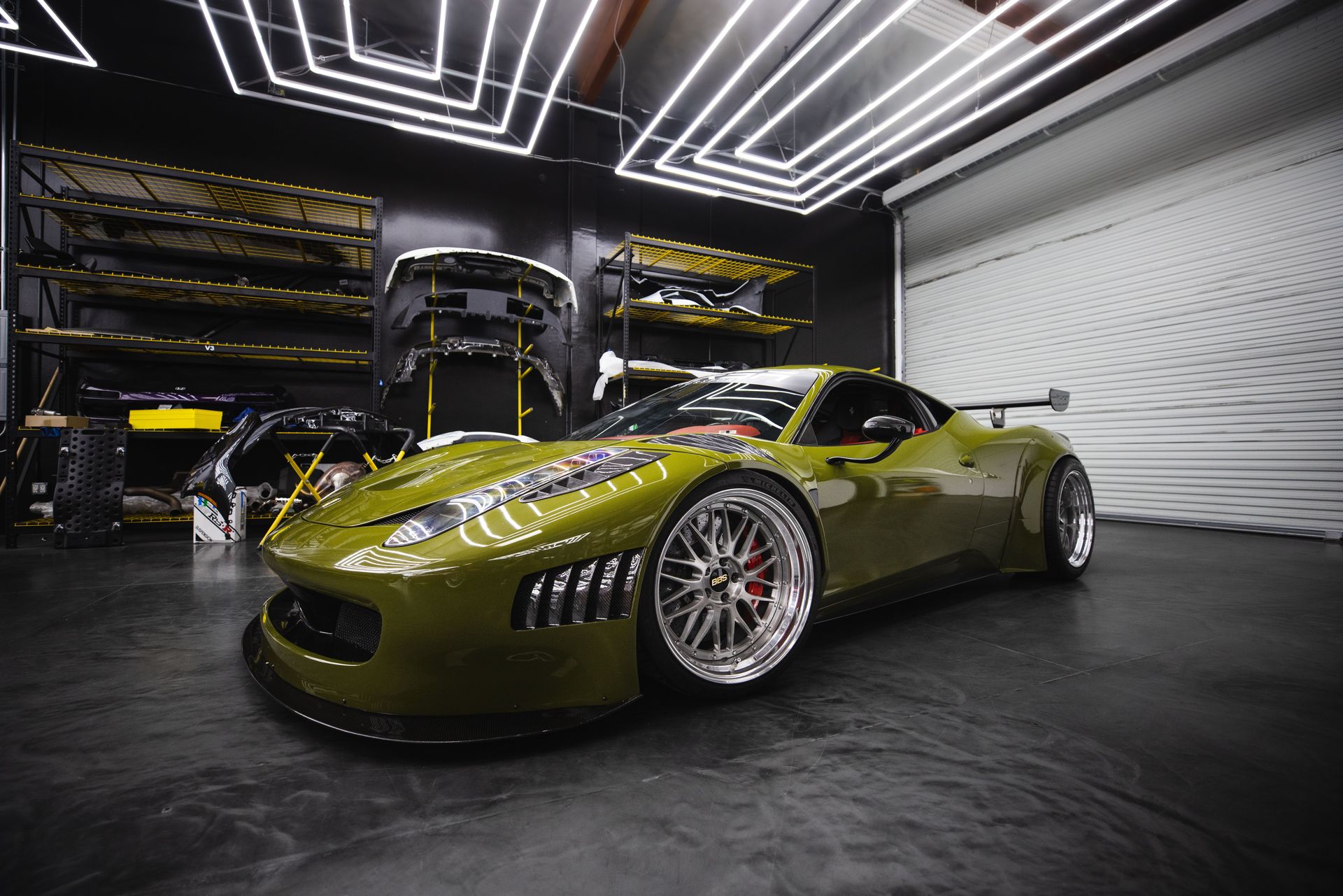 A sleek green sports car with custom modifications in a modern garage workshop.