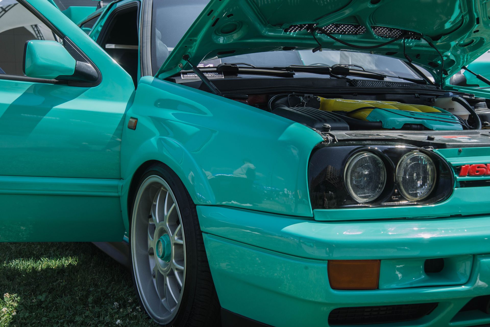 A vibrant teal classic car with the hood open showcasing the engine at an outdoor show.
