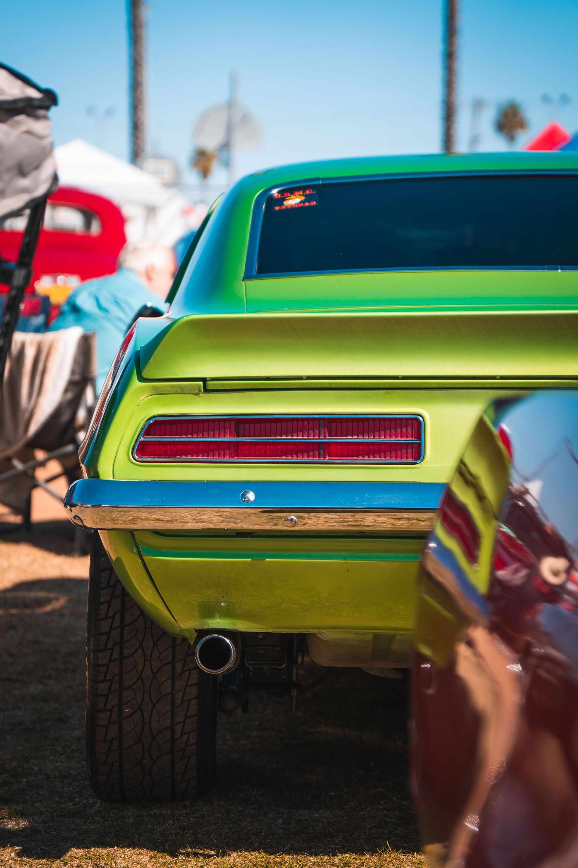 Bright green classic car tail view at an outdoor vehicle exhibition during daytime.